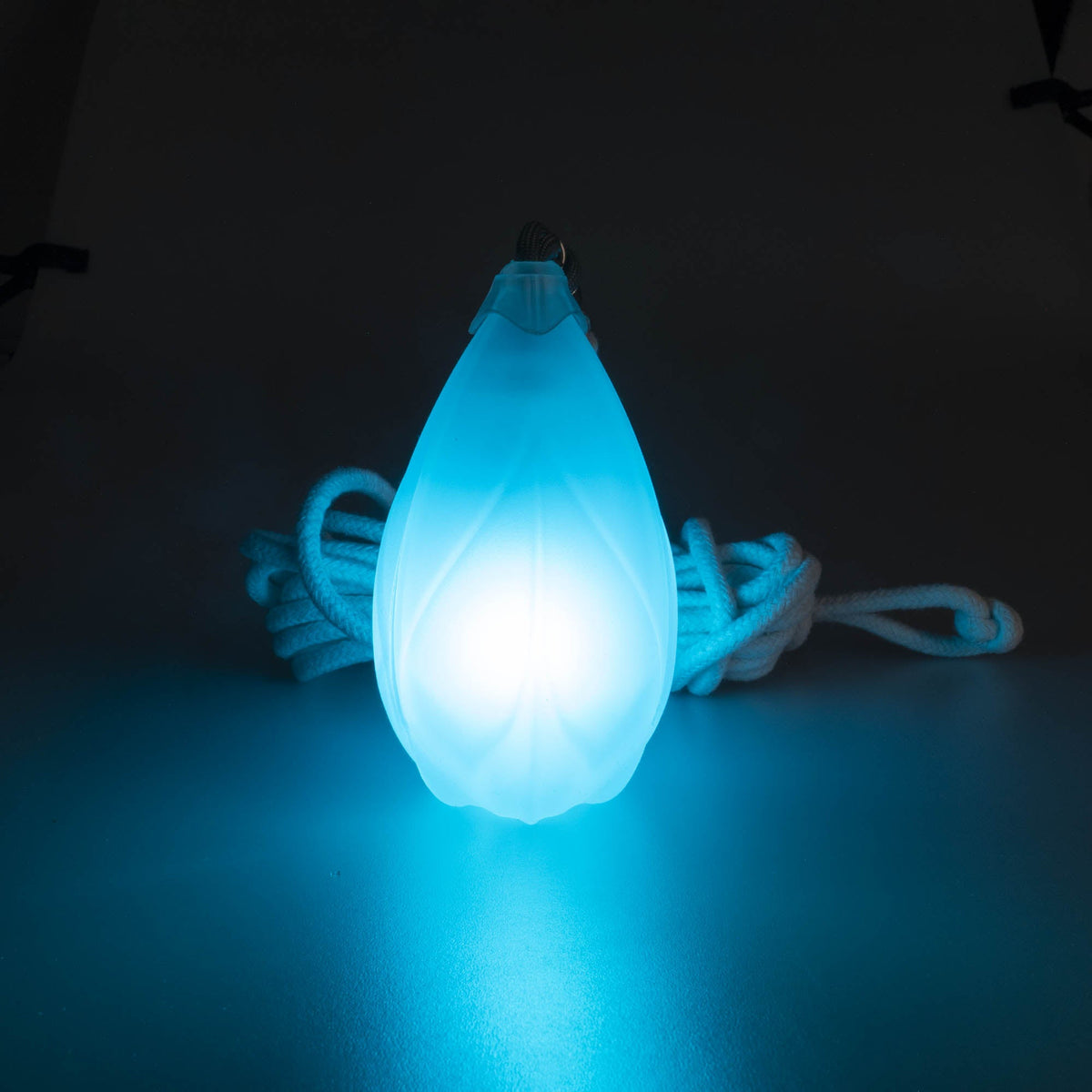 Flowtoys pod dart V2 glowing blue in a dark background with cord behind