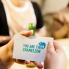 Person holding a card with 'You Are The Chameleon' text and logo.