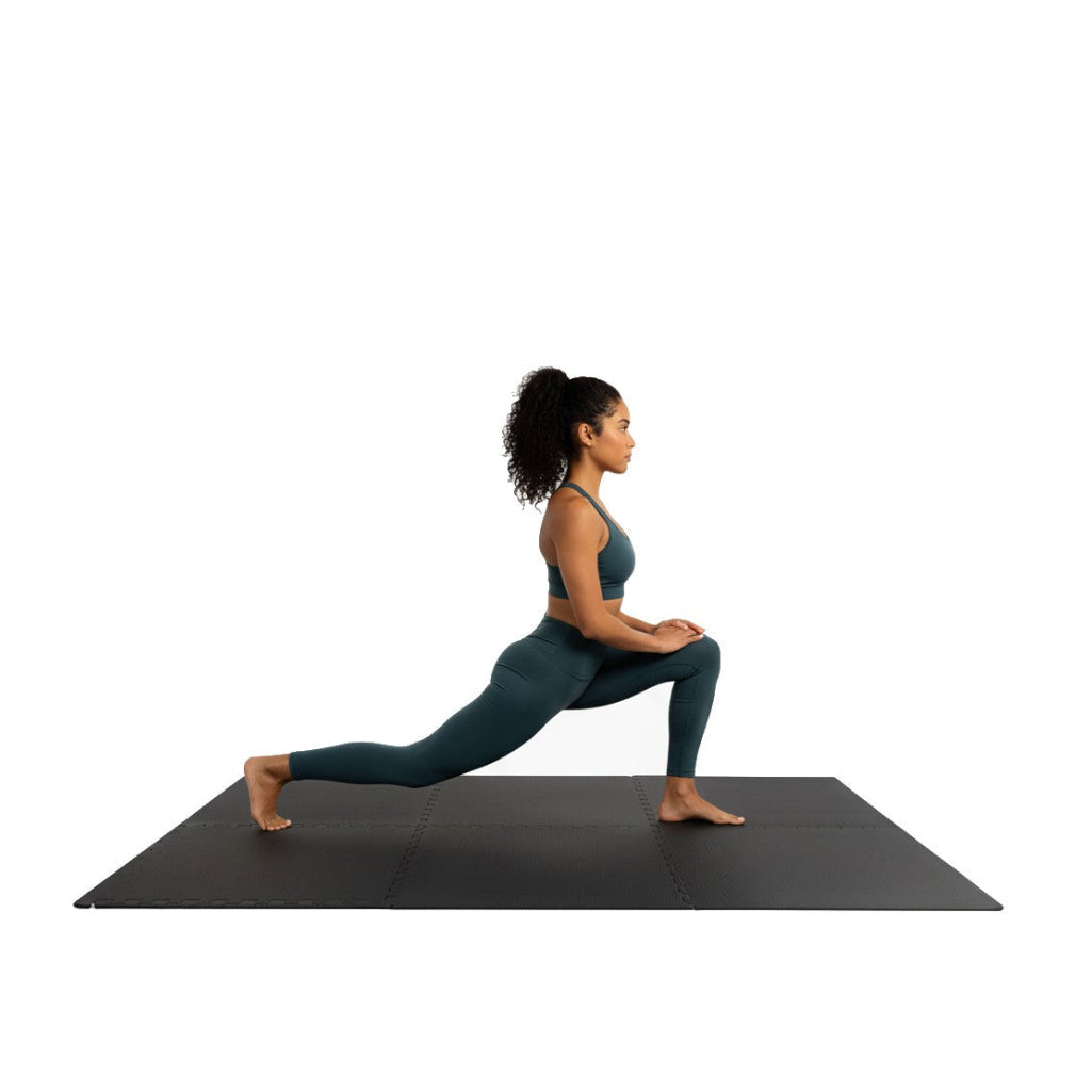 Woman performing a yoga pose on a black mat with a white background