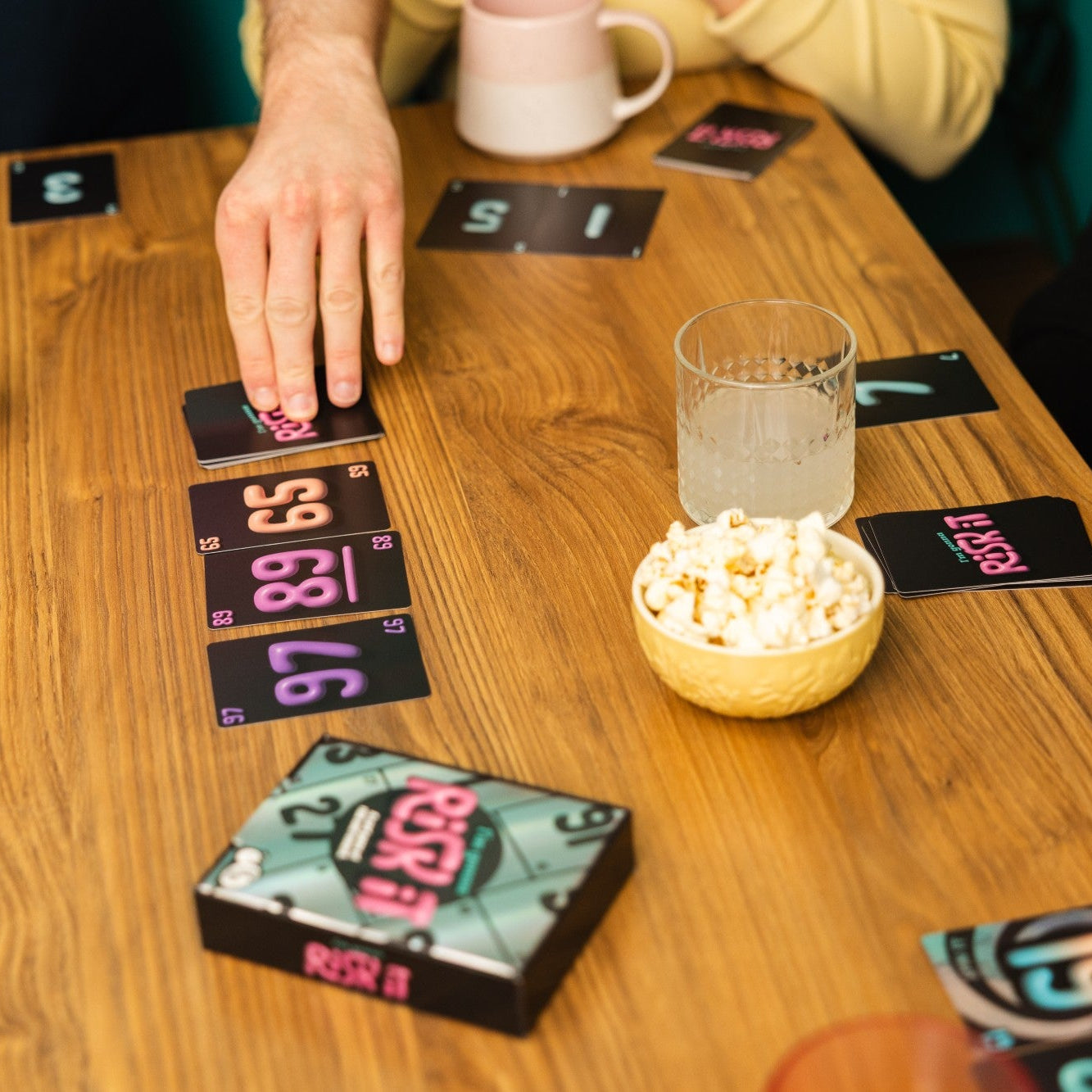 People playing a card game with cards and snacks on a wooden table.